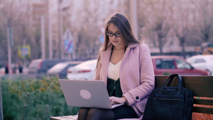 坐在长椅上和在城市公园背景中使用笔记本电脑的妇女16秒视频