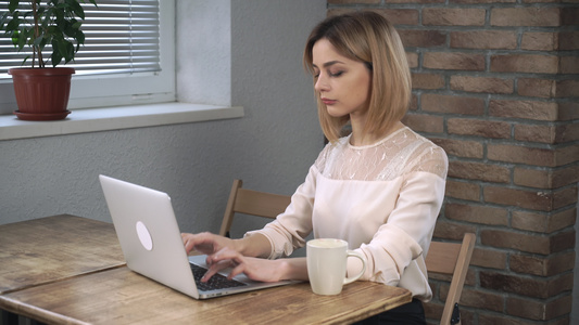 在笔记本上工作的女人喝着咖啡微笑在相机上视频