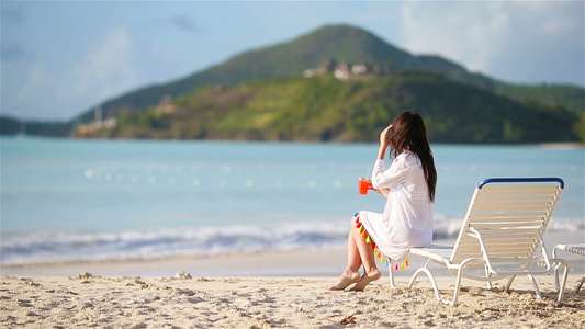 白沙滩上有鸡尾酒杯的年轻女子坐在阳光下视频