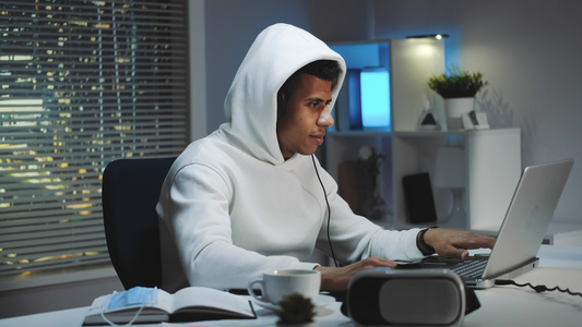 晚上穿着白色连帽衫和耳机在电脑上玩游戏的游戏玩家视频