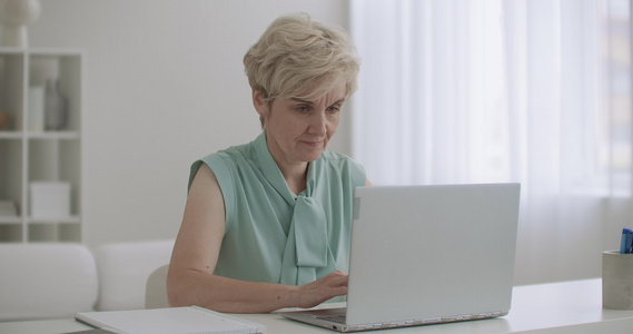 年老的女会计师在办公室用笔记本电脑工作妇女正在键盘视频