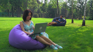 黑发女孩坐在公园懒人沙发上看笔记本电脑上工作18秒视频