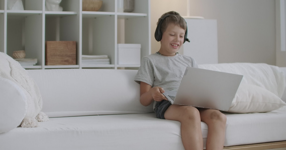 快乐的男孩坐在家里沙发上和一个人通过互联网愉快地交谈视频