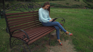一个年轻女孩坐在公园的长椅上翻平板电脑上的页纸11秒视频
