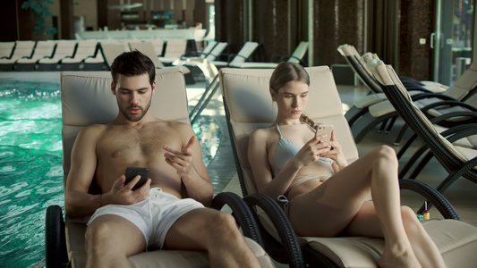 年轻夫妇在泳池附近看手机[相邻地方]视频