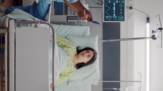 垂直视频生病妇女躺在床上而美国护士分析X光骨骼的前视镜视频