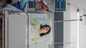 垂直视频生病妇女躺在床上而美国护士分析X光骨骼的前视镜15秒视频