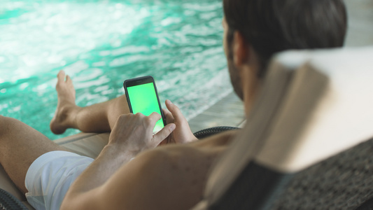 年轻人在手机泳池边滚动握智能机[品牌手机]视频