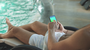 在酒店的游泳池手握着绿色屏幕手机的男人19秒视频