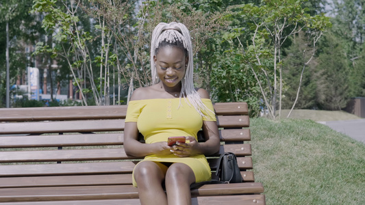 利用坐在长椅上的手机用白胸罩的时髦妇女视频