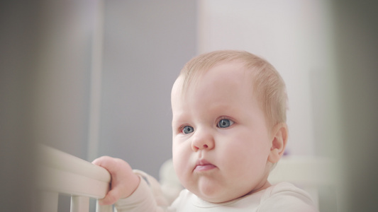 婴儿用蓝眼睛面对可爱的婴儿脸孔站在床上看周围视频