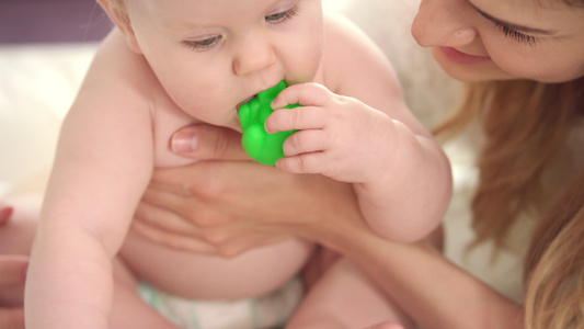 小婴儿坐在妈妈的怀抱里穿尿布玩着绿色玩具视频