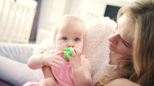 美丽的女婴坐在母亲的怀抱中嘴里带着玩具的托德勒女孩视频