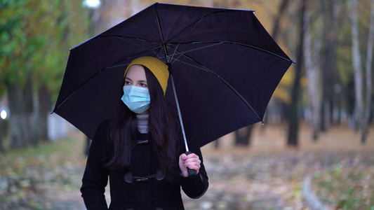 一位戴着防护面具的年轻女子在雨伞下在公园里散步下雨天视频