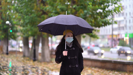 一位戴着防护面具的年轻女子在雨伞下在公园里散步下雨天视频