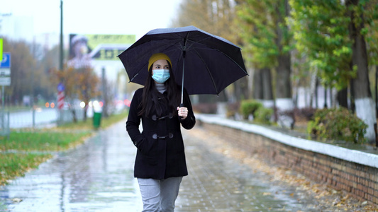 一位戴着防护面具的年轻女子在雨伞下在公园里散步下雨天视频