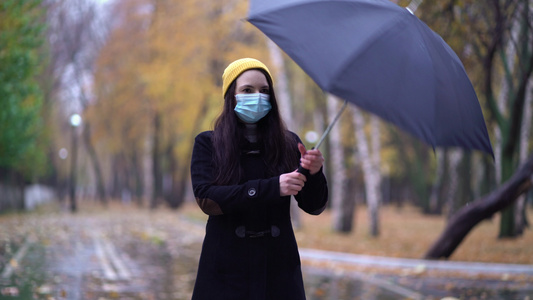 一位戴着防护面具的年轻女子在雨伞下在公园里散步下雨天视频