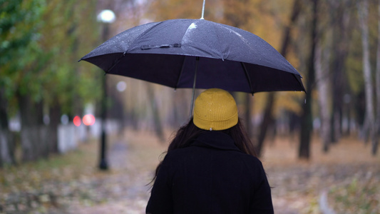 一位戴着防护面具的年轻女子在雨伞下在公园里散步视频