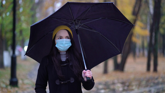 一位戴着防护面具的年轻女子在雨伞下在公园里散步下雨天视频