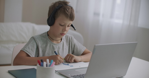 在大流行中在家上学小男孩正在用耳机听老师讲课用笔记本电脑视频