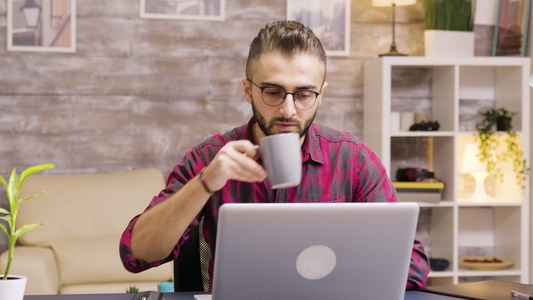 英俊的企业家在笔记本电脑上工作时喝一小口咖啡视频