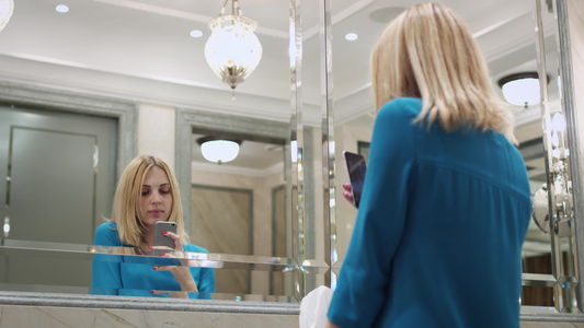美丽的女人在浴室手机前镜上拍自视频
