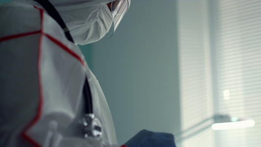 医生穿着医用防护服在医院病房中手持平板电脑视频