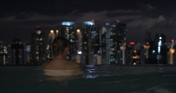 在摩天大楼屋顶的游泳池里女性和男性在夜市风景中环绕着视频