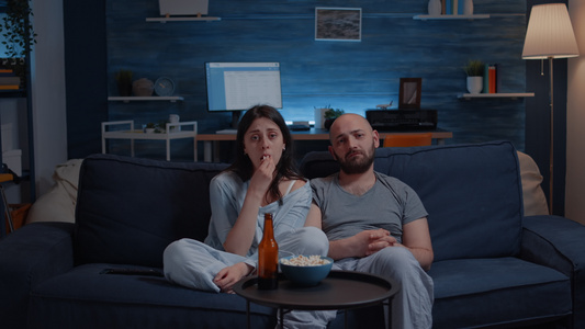 坐在沙发上哭泣的一对情侣在电视上观看戏剧电影视频