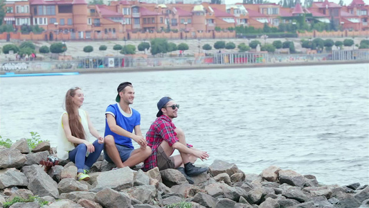 三个朋友坐着笑笑向河上扔石头视频