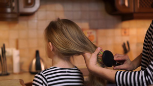 在舒适的木制厨房家中母亲梳刷女儿女孩长长的金发穿着18秒视频