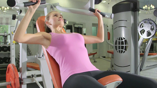在健身房中年轻女人对胸压机举重视频