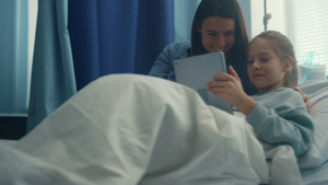 微笑的妈妈探望女儿在医院病房里一起玩平板电脑9秒视频