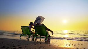 母亲和儿子坐在沙滩甲板椅上面对日落26秒视频