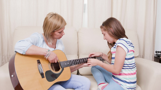 起居室的母亲和女儿学习用音响吉他弹奏音乐视频