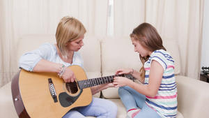起居室的母亲和女儿学习用音响吉他弹奏音乐18秒视频