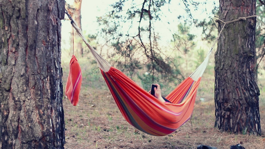 吊床放松在森林吊床上使用智能手机的年轻女子视频