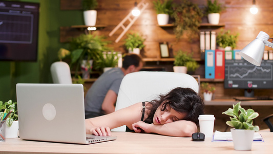 妇女在工作时在工作场所睡觉而她的同事正在工作视频