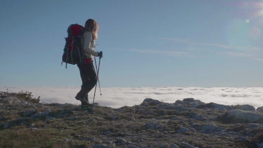 阳光明媚的日子里背着背包和登山杖的年轻女子正在云层视频