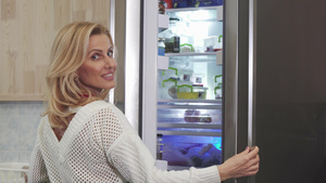 美丽的女人对着摄影机微笑在厨房打开冰箱的笑容8秒视频