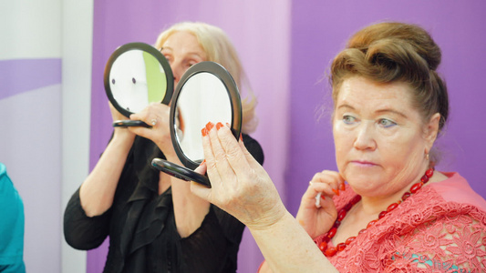 上化妆课的老年妇女看着手中的镜子尝试新的技能视频