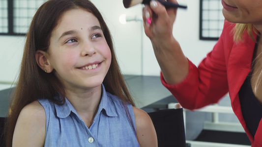 一个漂亮小女孩在她妈妈脸上化妆时微笑的特写视频