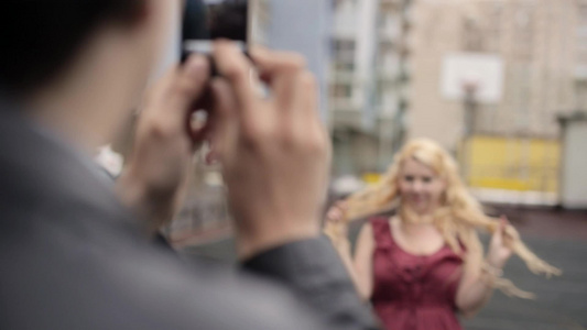 年轻男子在手机上拍摄女友在街上玩得开心的手机照片视频