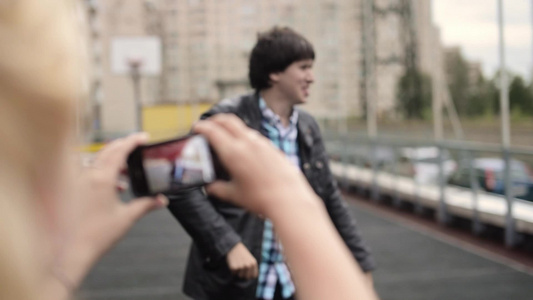 年轻女孩在手机上拍摄男朋友在街上玩乐的男友照片视频