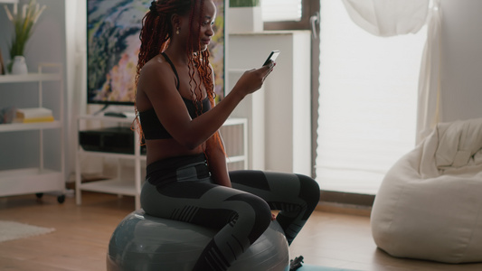 坐在健身球上的黑皮肤弱瘦女人在电话中写信息视频