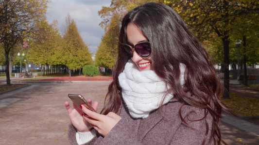 年轻美丽笑脸的黑发女人在太阳镜中长发在城市公园使用视频