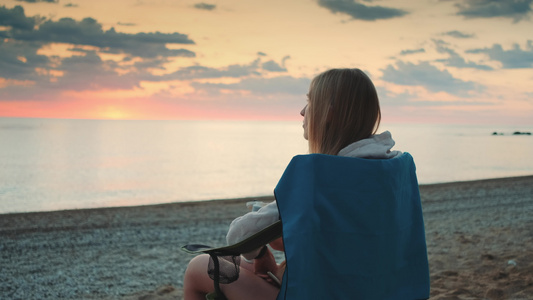女人喝热水坐在沙滩上的露营椅上视频
