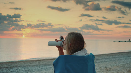 年轻女子喝热杯酒在日出前坐在沙滩上视频