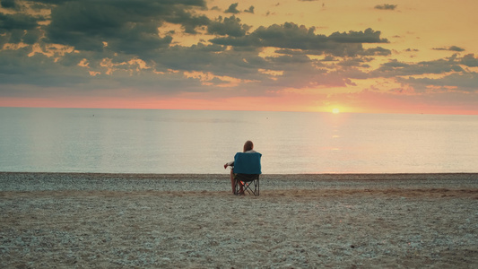 坐在折叠的旅游椅上的海面上看着女孩仰慕日落视频