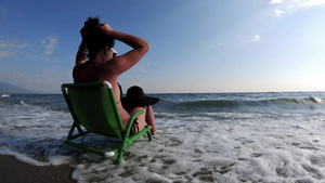穿着比基尼的漂亮年轻美女戴着帽子坐在沙滩上的椅子上28秒视频